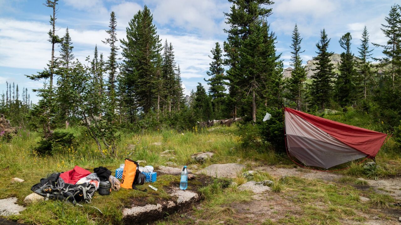 Campingplatz in den Bergen mit aufgebautem Tarp und ausgebreiteter Ausrüstung