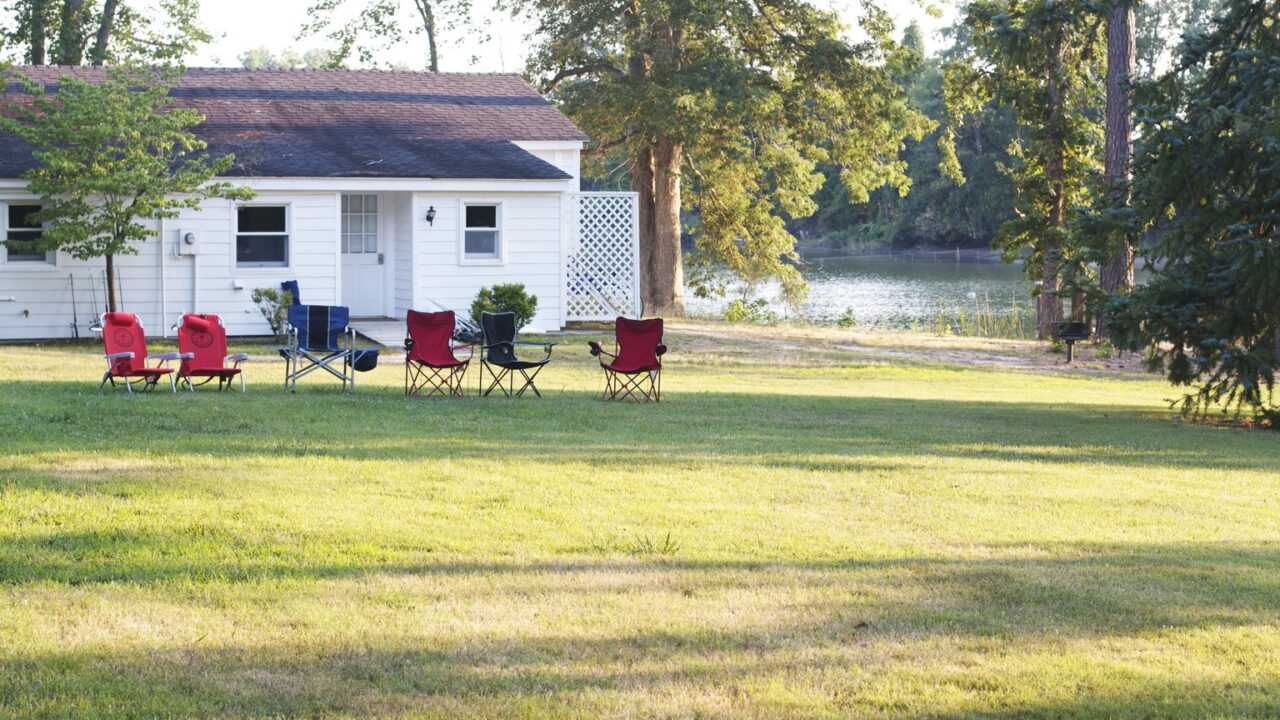 Campingstühle und Falttische auf einer Wiese am See im Abendlicht