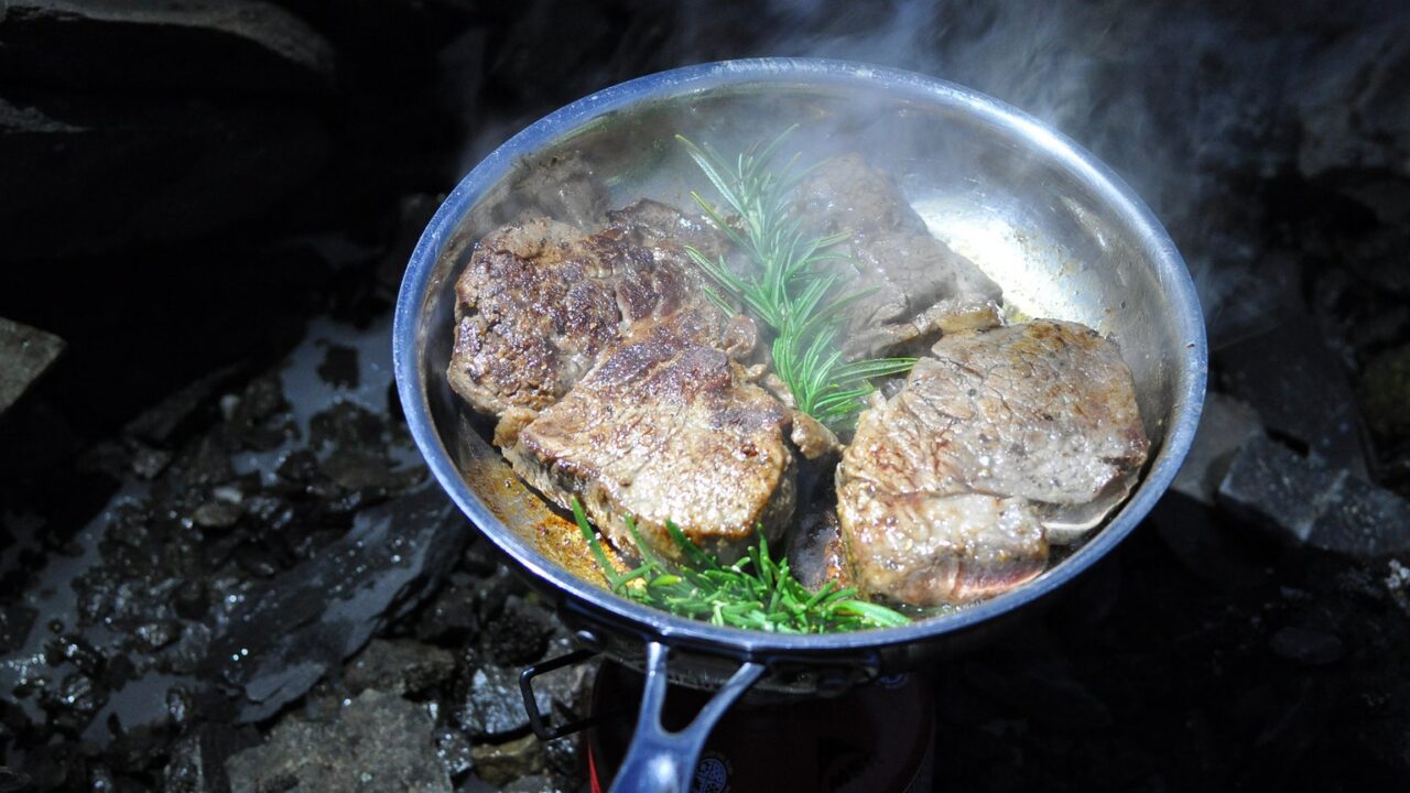 Fleisch mit Rosmarin brät in der Pfanne auf einem Campingkocher