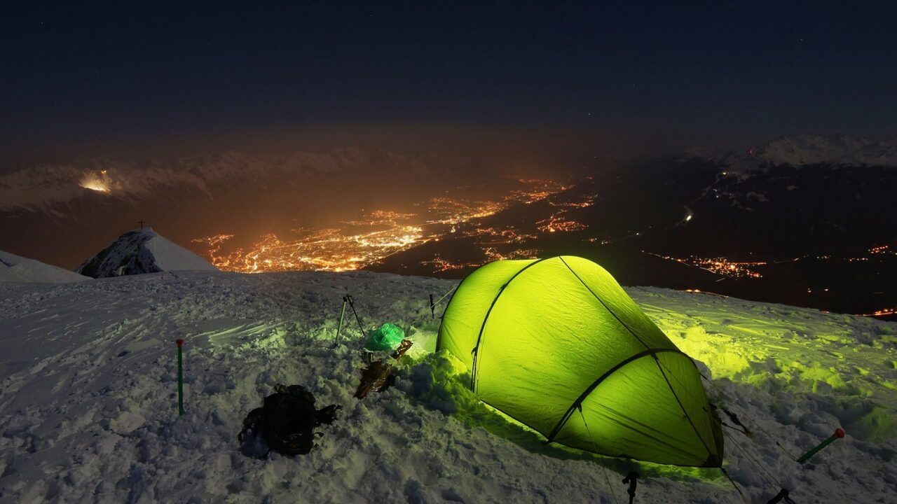 Beleuchtetes Zelt im Schnee auf einem Berg über einem Tal in der Dämmerung